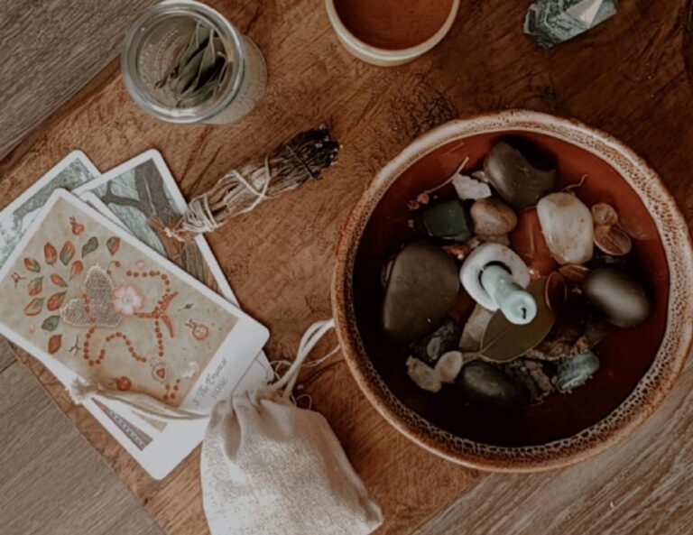 a money bowl off-center with two tarot cards to the left. A green candle in the center of the bowl surrounded by crystals and items. other necessities fill the spell casting altar