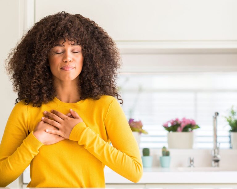Black woman curly hair yellow tshirt hands over heart