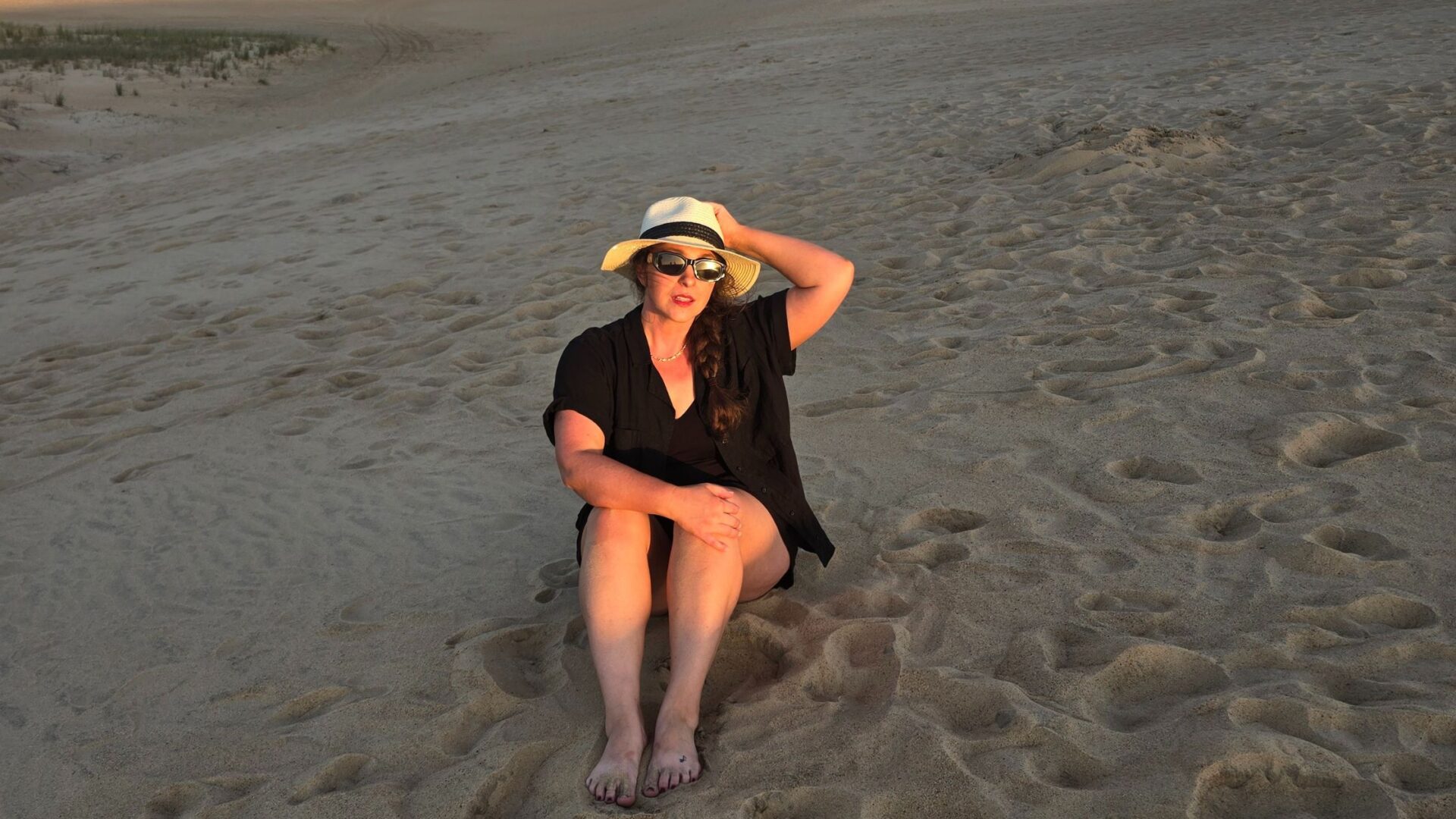 Girl sitting on the sand in a hat and sunglasses
