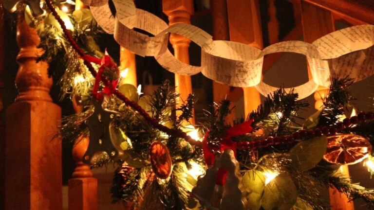 Warmly lit Yule garland with evergreen branches, dried oranges, paper chains, and silver ornaments along a wooden banister — traditional Green Witch holiday décor celebrating the Winter Solstice.