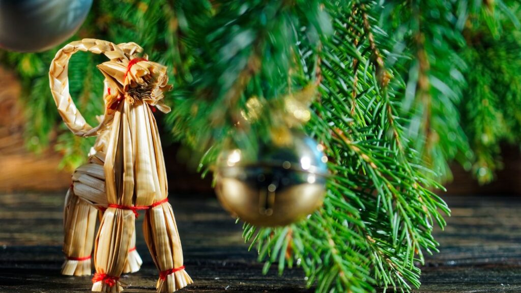 Traditional straw Yule goat ornament beneath evergreen branches, symbolizing winter folklore and December solstice traditions.